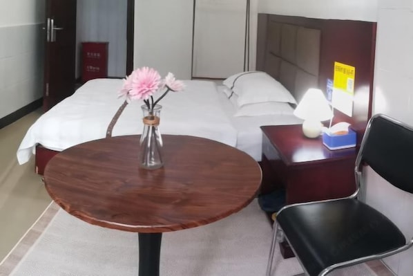 Habitación de hotel con una cama, una pequeña mesa redonda de madera con un jarrón de flores, un escritorio con una lámpara y una silla.