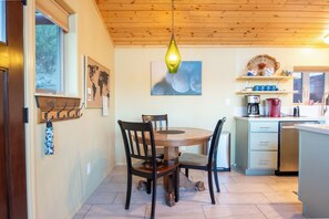 Une table de salle à manger en bois avec des chaises, un luminaire suspendu, une carte du monde et une machine à café dans une cuisine.
