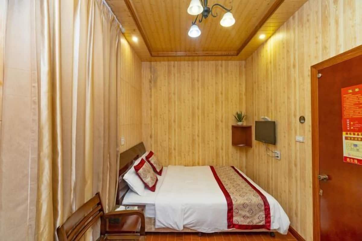 Habitación con paneles de madera, una cama, una silla, un estante pequeño con una planta y una puerta con un letrero rojo.