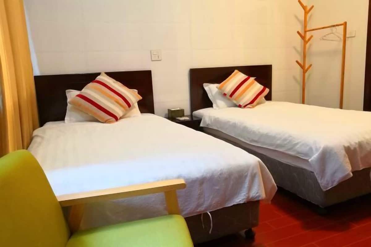 Dos camas individuales con ropa de cama blanca y almohadas a rayas, un perchero de madera y una silla verde.