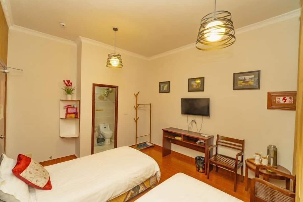 Habitación de hotel con dos camas, un escritorio, una silla, un televisor y una estantería con objetos.