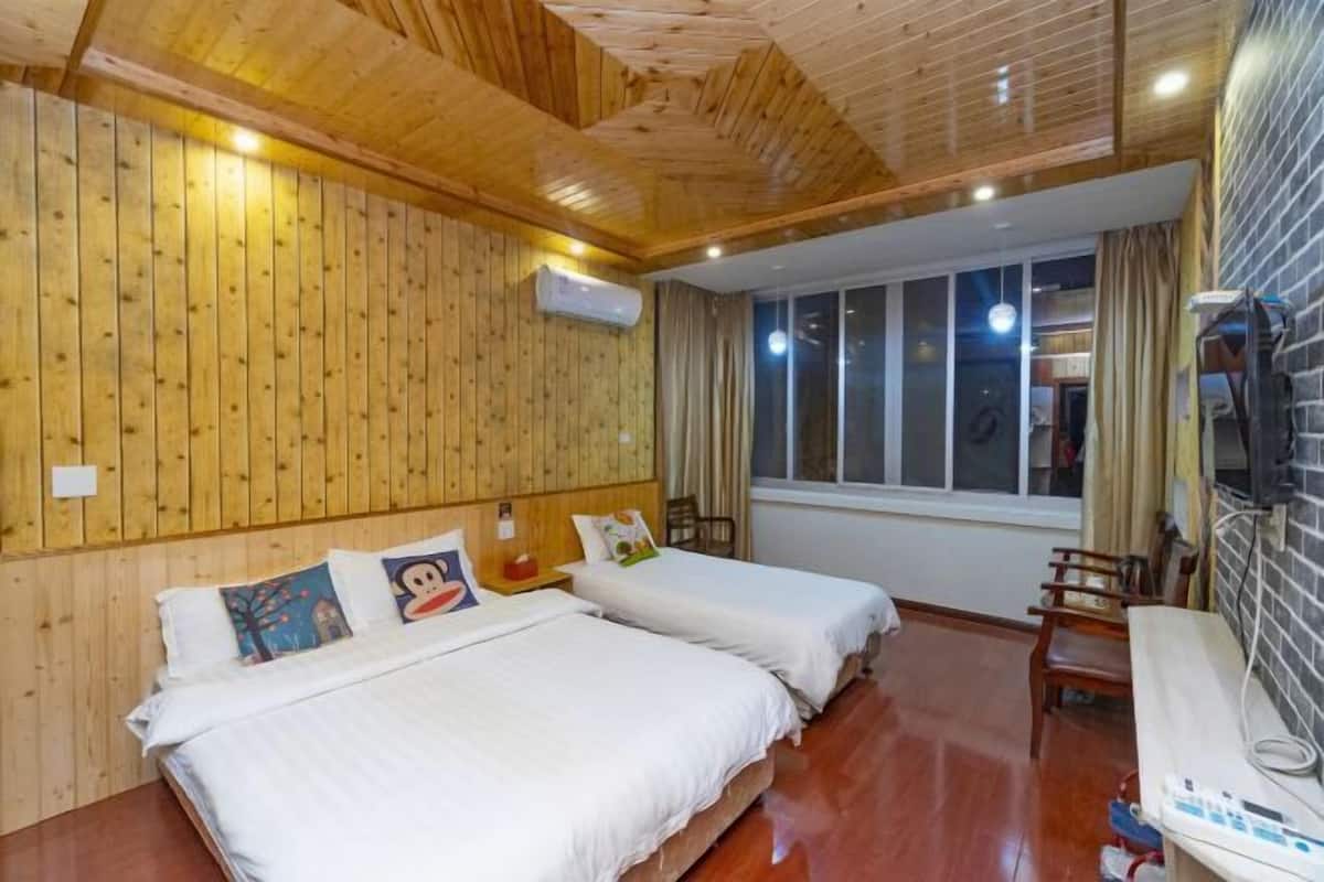 Una habitación con paredes de paneles de madera, dos camas con ropa blanca, una ventana con cortinas, techo de madera y un televisor en la pared.