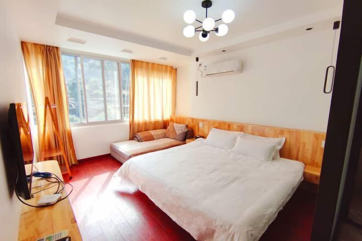 Habitación de hotel con una cama grande, un sofá, un televisor y un ventanal con cortinas.