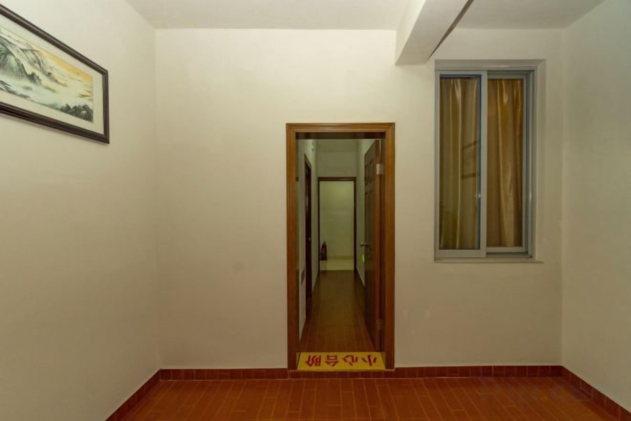 A hallway with a wooden door, a window with curtains, and a framed picture on the wall.