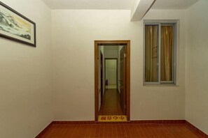Un corridoio con una porta in legno, una finestra con tende e un quadro appeso al muro.