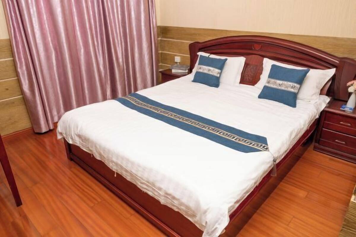 A neatly made bed with a white and blue bedspread, a wooden headboard, and a nightstand with a lamp.