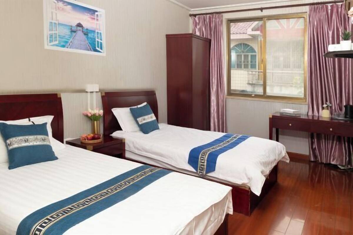 A hotel room with two beds, a wooden wardrobe, a desk, and a window with curtains.