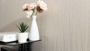 Un vase blanc orné de fleurs et une petite plante sont posés sur une table noire, le tout se détachant sur un mur à la texture marquée.