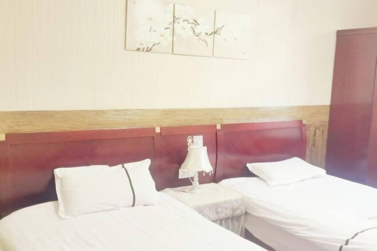 A hotel room with two beds, a wooden headboard, a nightstand with a lamp, and a wall-mounted artwork.