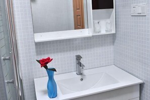 A bathroom with a white sink, a blue vase with a red flower, and a mirror above the sink. - Haoke Renjia Inn (Suzhou)
