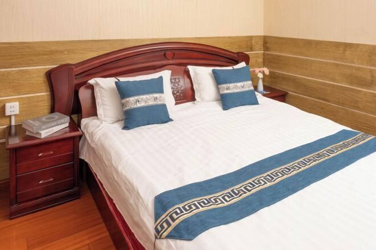 A neatly made bed with a decorative headboard, a bedside table with a telephone, and a wall with a wooden panel design.
