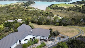 A house with a sloped roof, surrounded by a garden with raised beds, near a coastal area with a road curving around the property. - Russell's Secluded Secret (Russell)
