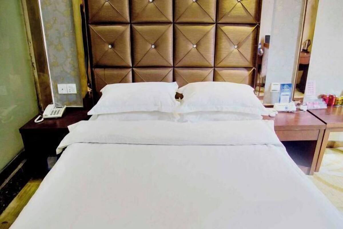 Habitación de hotel con cabecera capitonada, cama con ropa blanca, mesita de noche con teléfono y pequeño escritorio con computadora y documentos.
