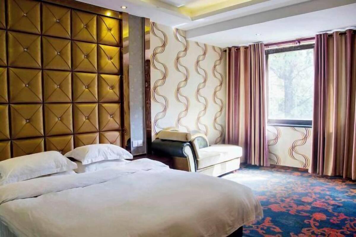 Habitación de hotel con una cama grande, un sofá, un papel pintado decorativo y una ventana con cortinas.