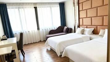 A hotel room with two beds, a desk, and a window with curtains.