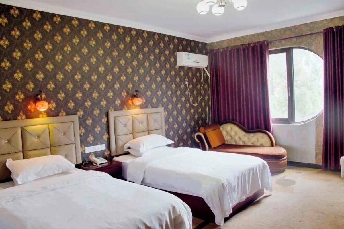 Habitación de hotel con dos camas, un sofá, un ventanal con cortinas y un equipo de aire acondicionado.
