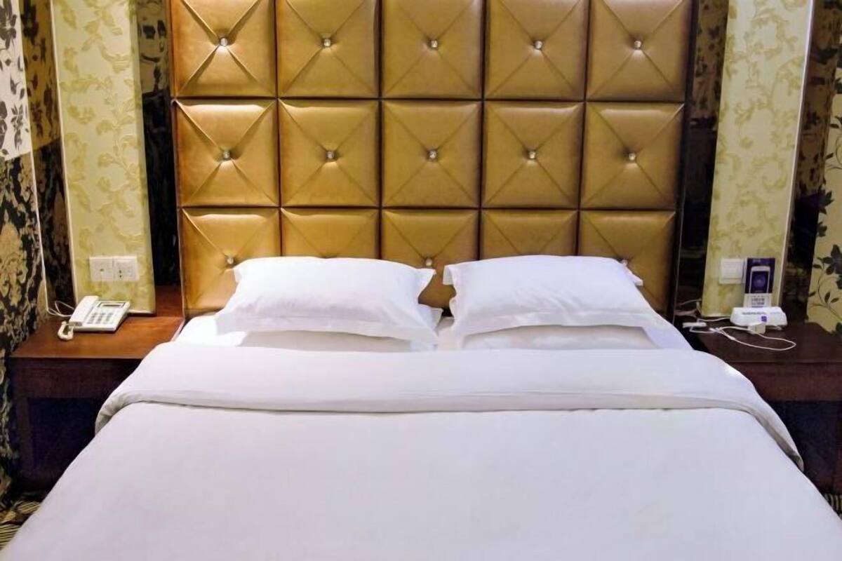 Habitación de hotel con cabecera capitonada, cama con ropa de cama blanca, teléfono en la mesita de noche y lámpara.