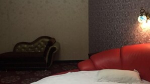 A room with a red sofa, a dark brown armchair, and a patterned wall. - Linyuan Hotel (Jinhua)