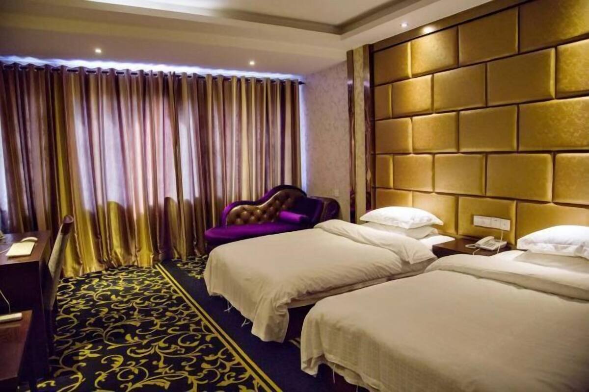 Habitación de hotel con dos camas, un escritorio, una silla y un ventanal con cortinas.