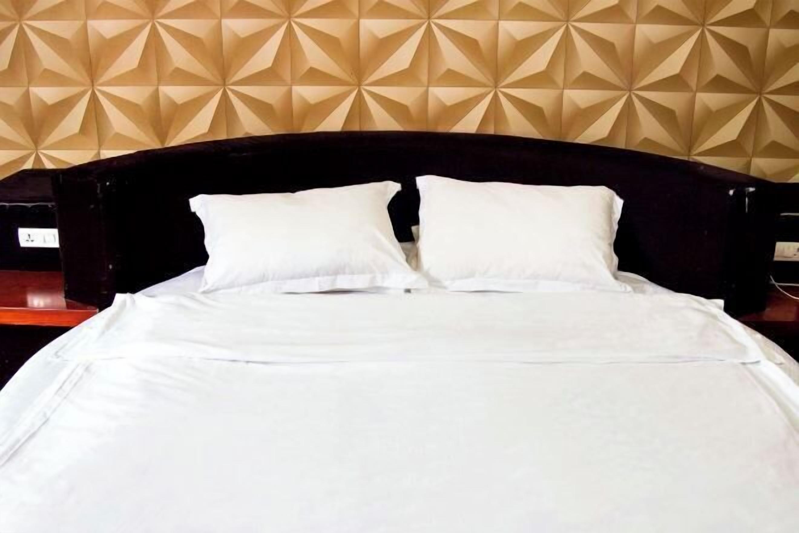 Una cama bien tendida con sábanas blancas y dos almohadas, frente a una pared con papel tapiz de diseño geométrico.