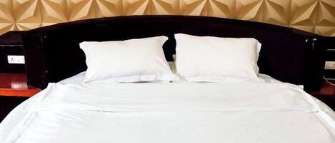Una cama bien tendida con sábanas blancas y dos almohadas, frente a una pared con papel tapiz de diseño geométrico.