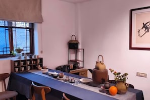 A dining area with a long table, chairs, and various kitchen items. - Tianyi Youth Hostel (Langzhong)