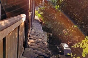 Un sendero de piedra que lleva a una estructura de madera con una mesa pequeña y una silla, rodeado de follaje.