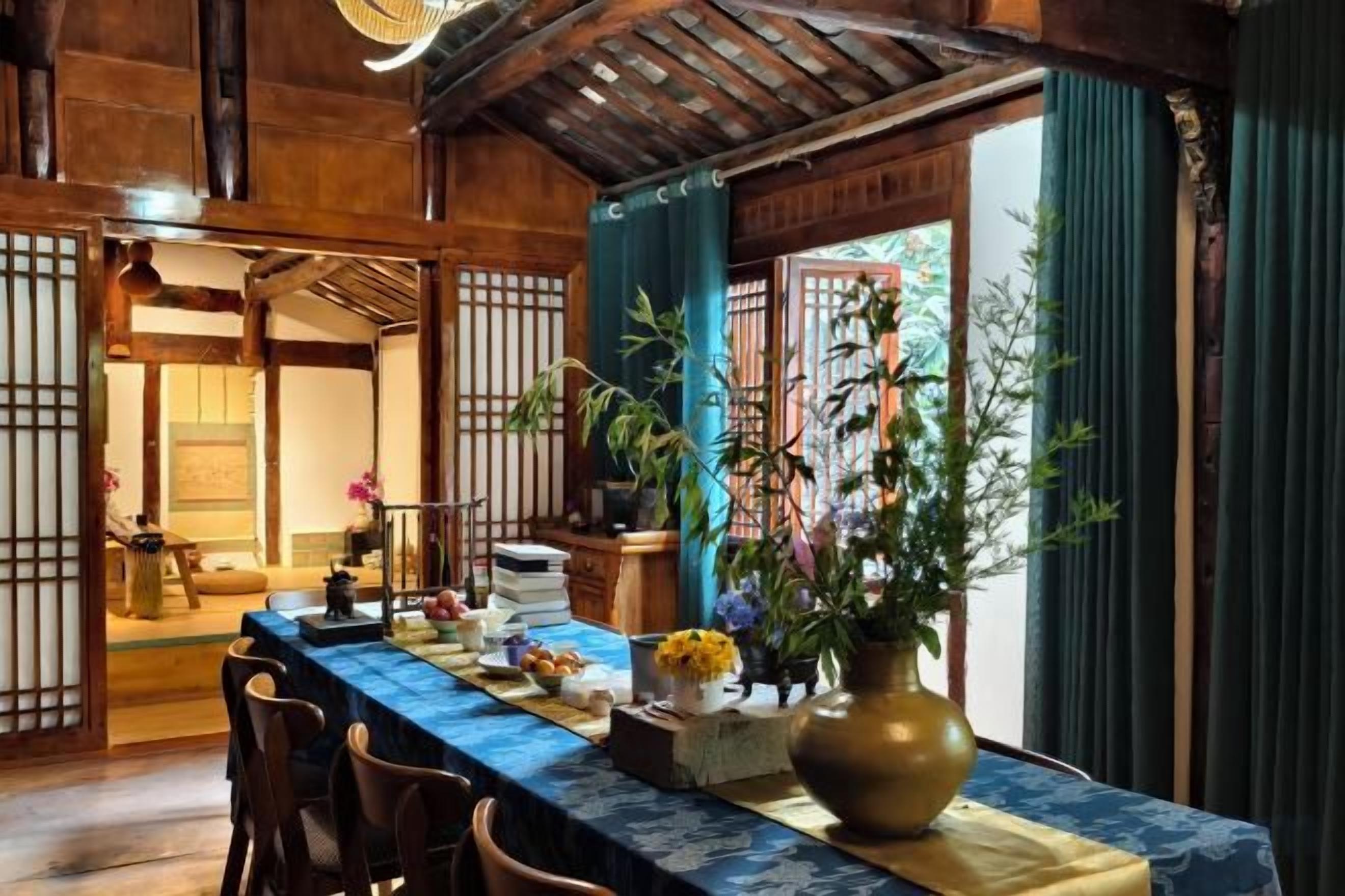 A traditional Japanese-style room with tatami flooring, a low table with a blue tablecloth, and a large vase of flowers.
