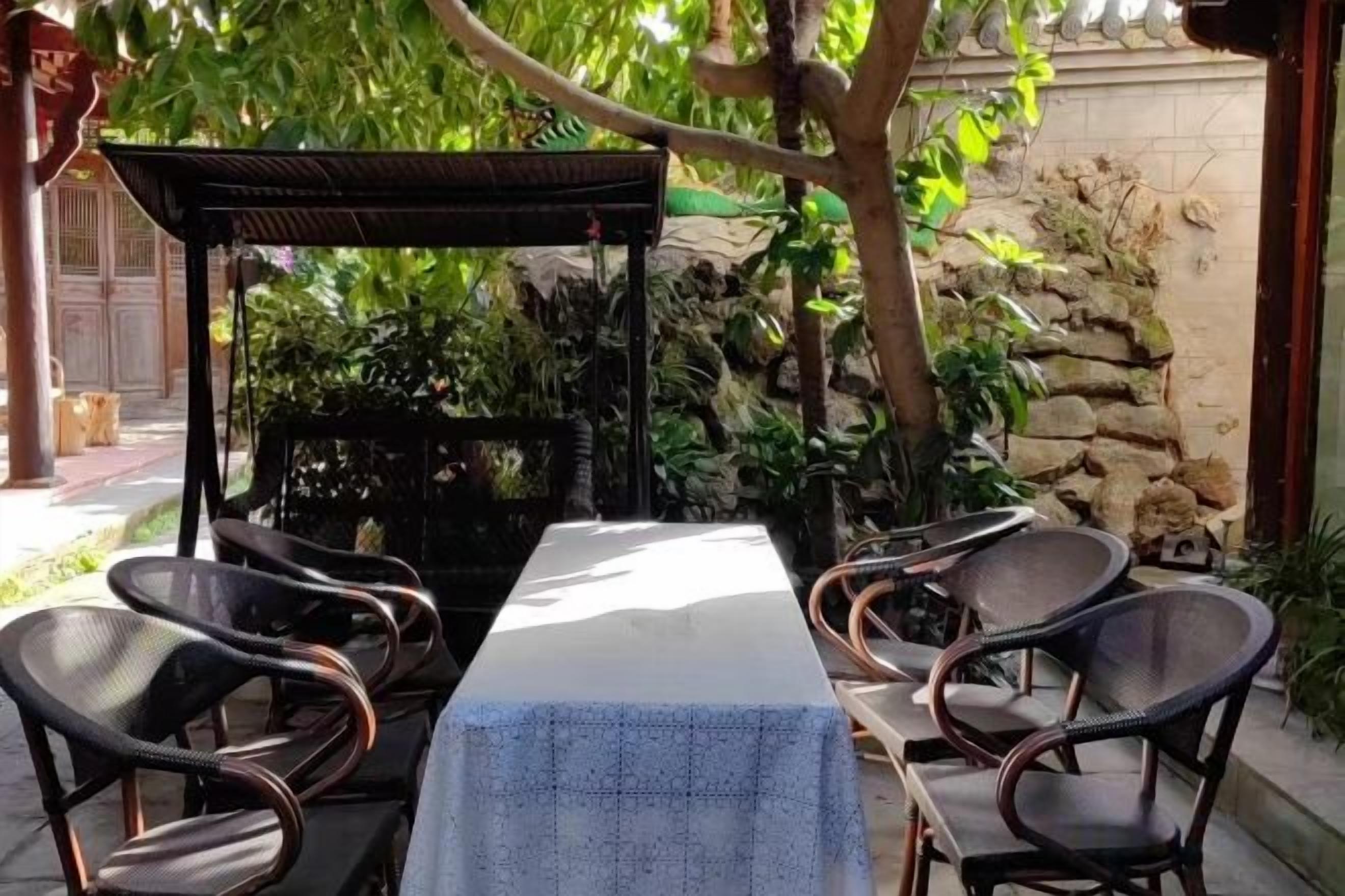 Un área de comedor al aire libre con una mesa y sillas, rodeada de plantas y un muro de piedra.