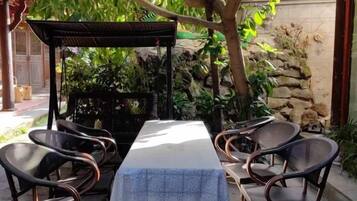 Un área de comedor al aire libre con una mesa y sillas, rodeada de plantas y un muro de piedra.