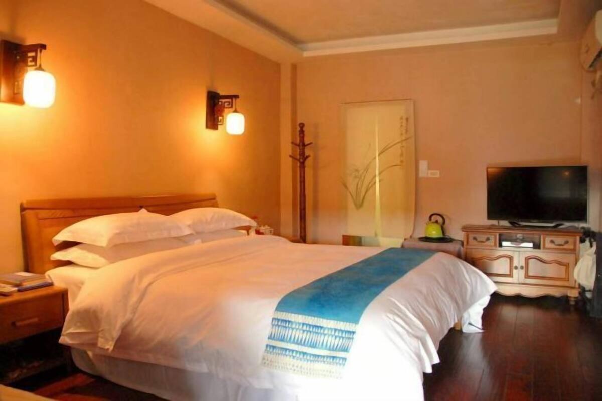 Una habitación de hotel con cama, mesita de noche, lámpara, perchero, armario y televisor.