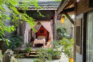 A traditional courtyard with a bed, potted plants, and a sign in a foreign language.