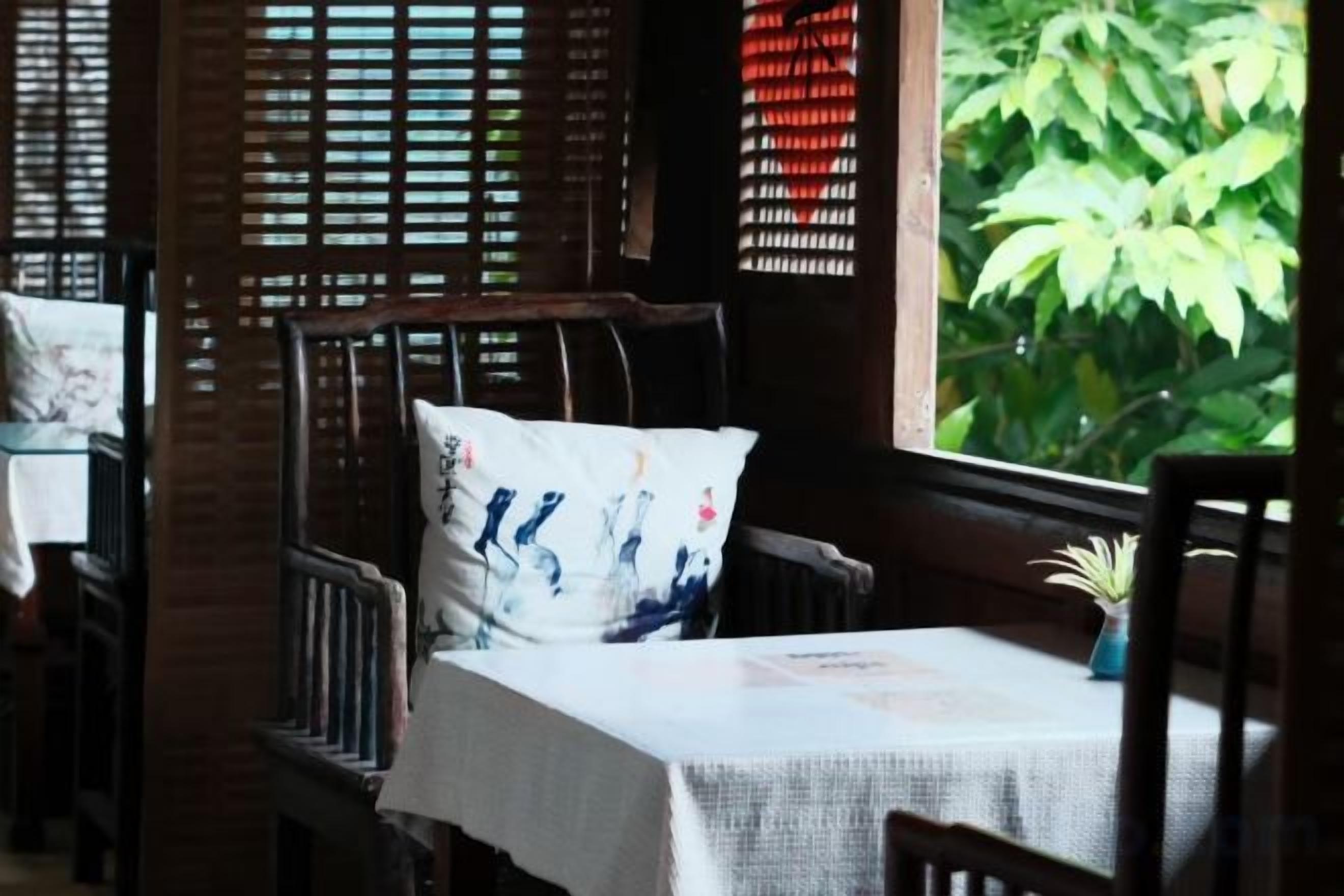 A dining area with wooden furniture, a table with a white tablecloth, and a view of greenery outside.
