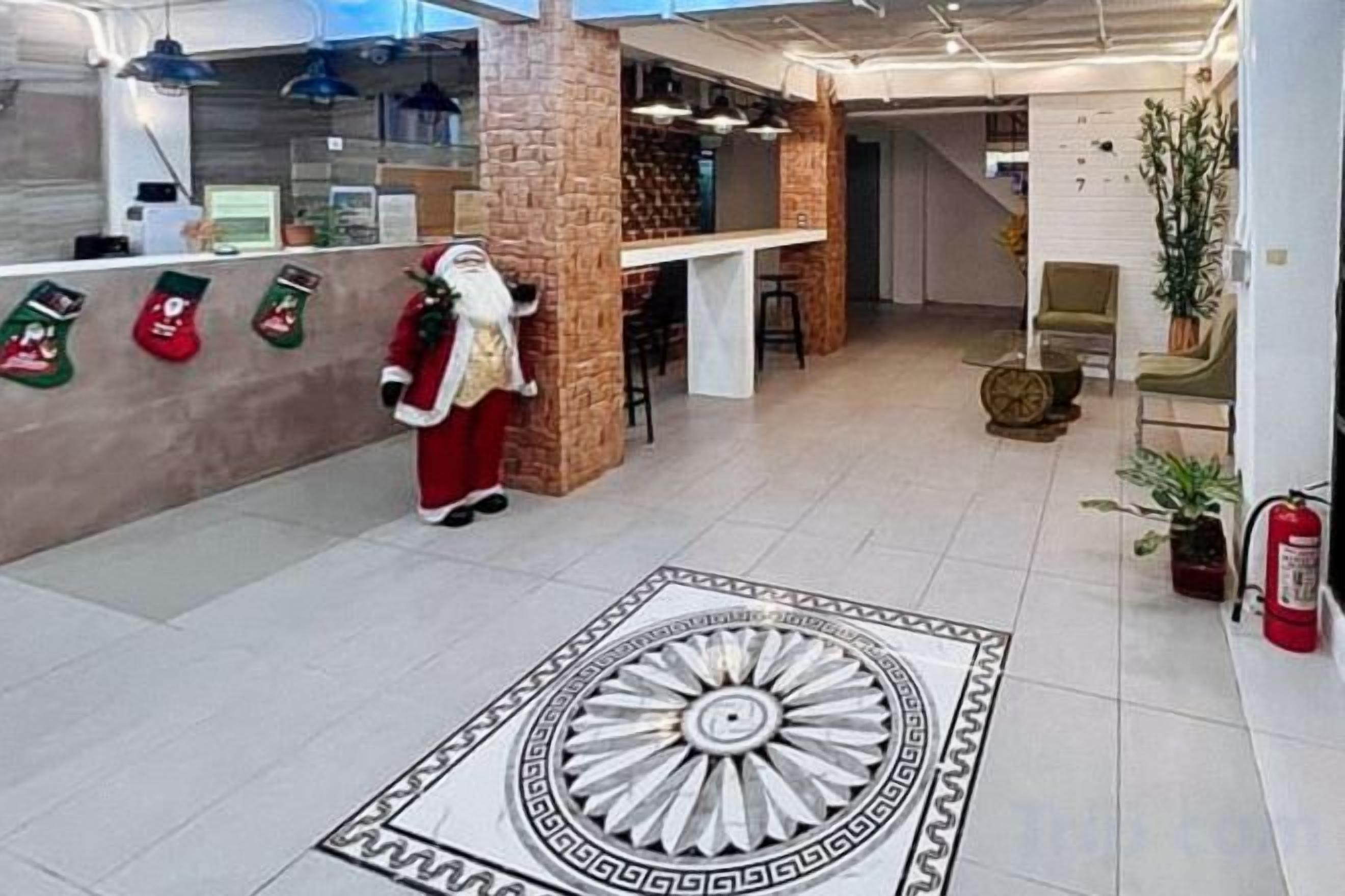Un hall d’hôtel doté d’un motif décoratif central sur le sol, d’un espace de réception avec un comptoir et d’un coin salon agrémenté d’une plante.