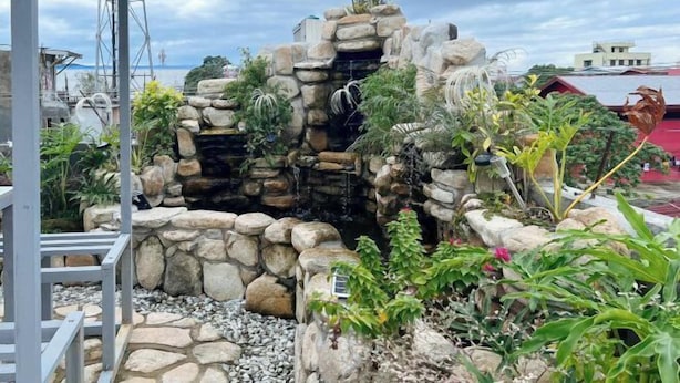 A rock garden with a waterfall, surrounded by various plants and rocks. - UrbanView @ Balzain East Tuguegarao City by RedDoorz (Tuguegarao)