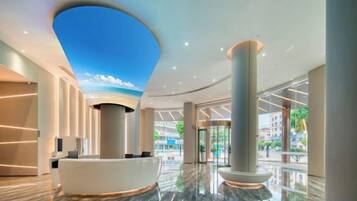 A hotel lobby with a reception desk, a large column, and a ceiling with a sky-like design.
