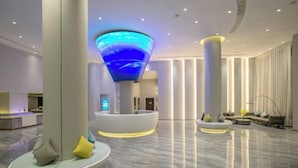 Een moderne lobby met een centraal zithoek, een grote verlichte sculptuur en een receptiebalie.