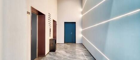 A hallway with a marble floor, a blue door at the end, and recessed lighting on the walls.