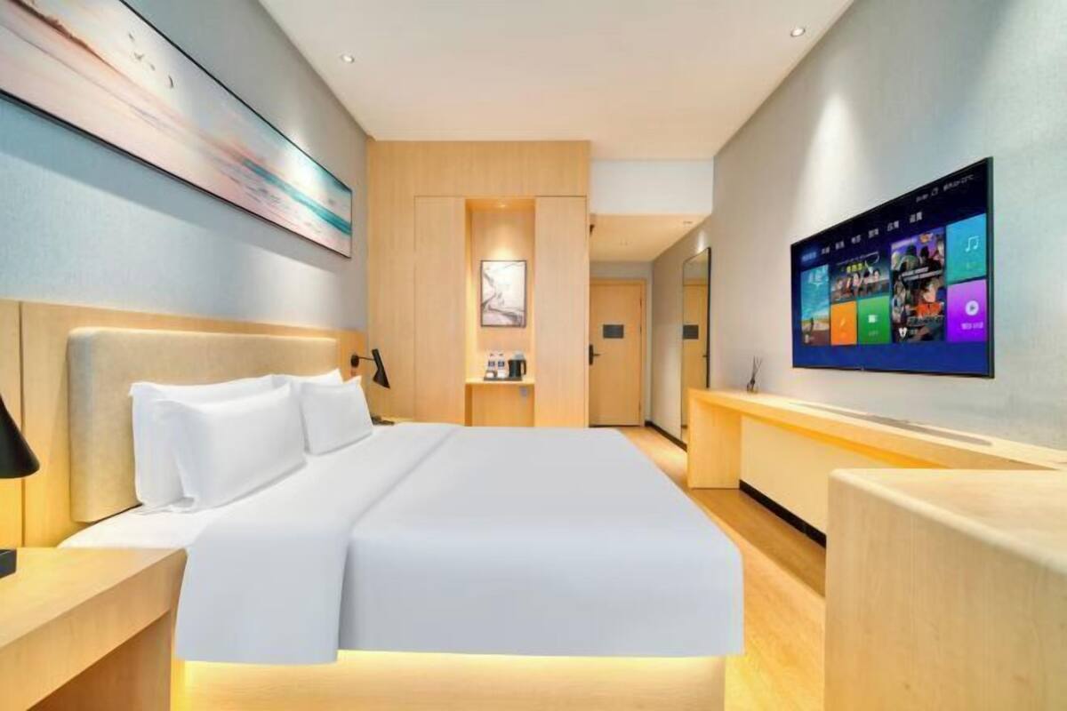 A modern hotel room with a large bed, a flat-screen TV, a desk, and a painting on the wall.