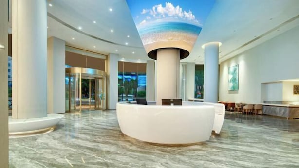Een moderne hotellobby met een receptiebalie, een marmeren vloer en een plafonddecoratie van een strandgezicht.