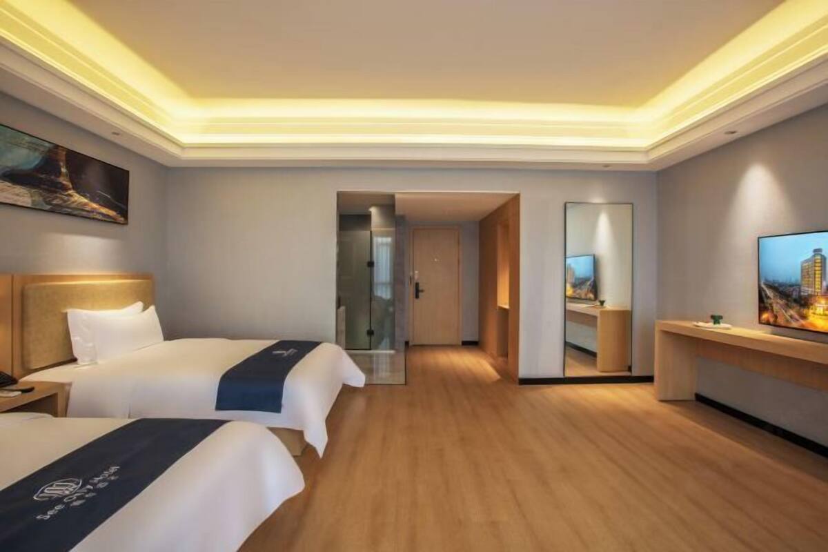 A hotel room with two beds, a desk, a mirror, and a painting on the wall.
