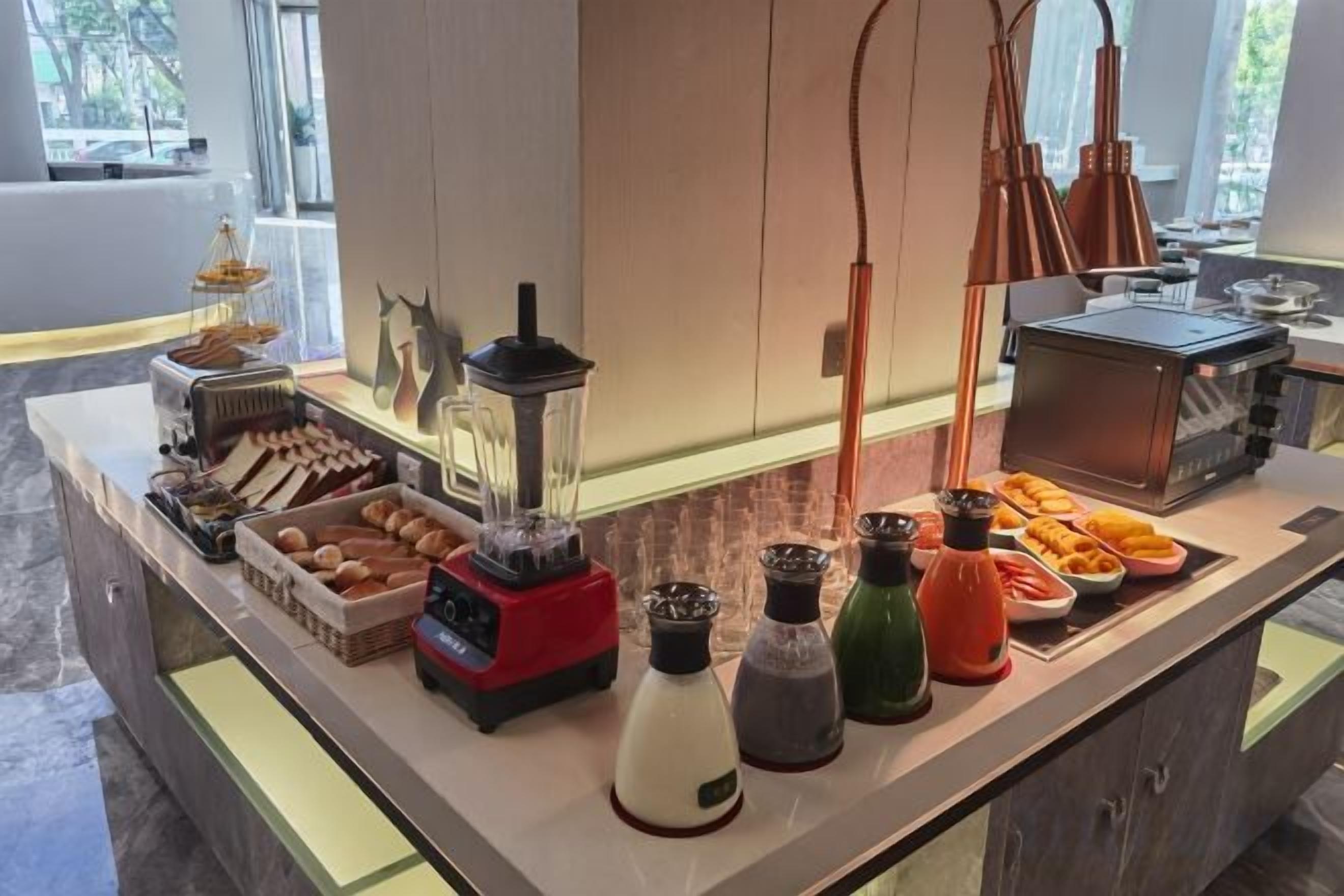 Un buffet proposant un mixeur, diverses sauces et condiments, ainsi qu’un assortiment de pains et de viennoiseries.