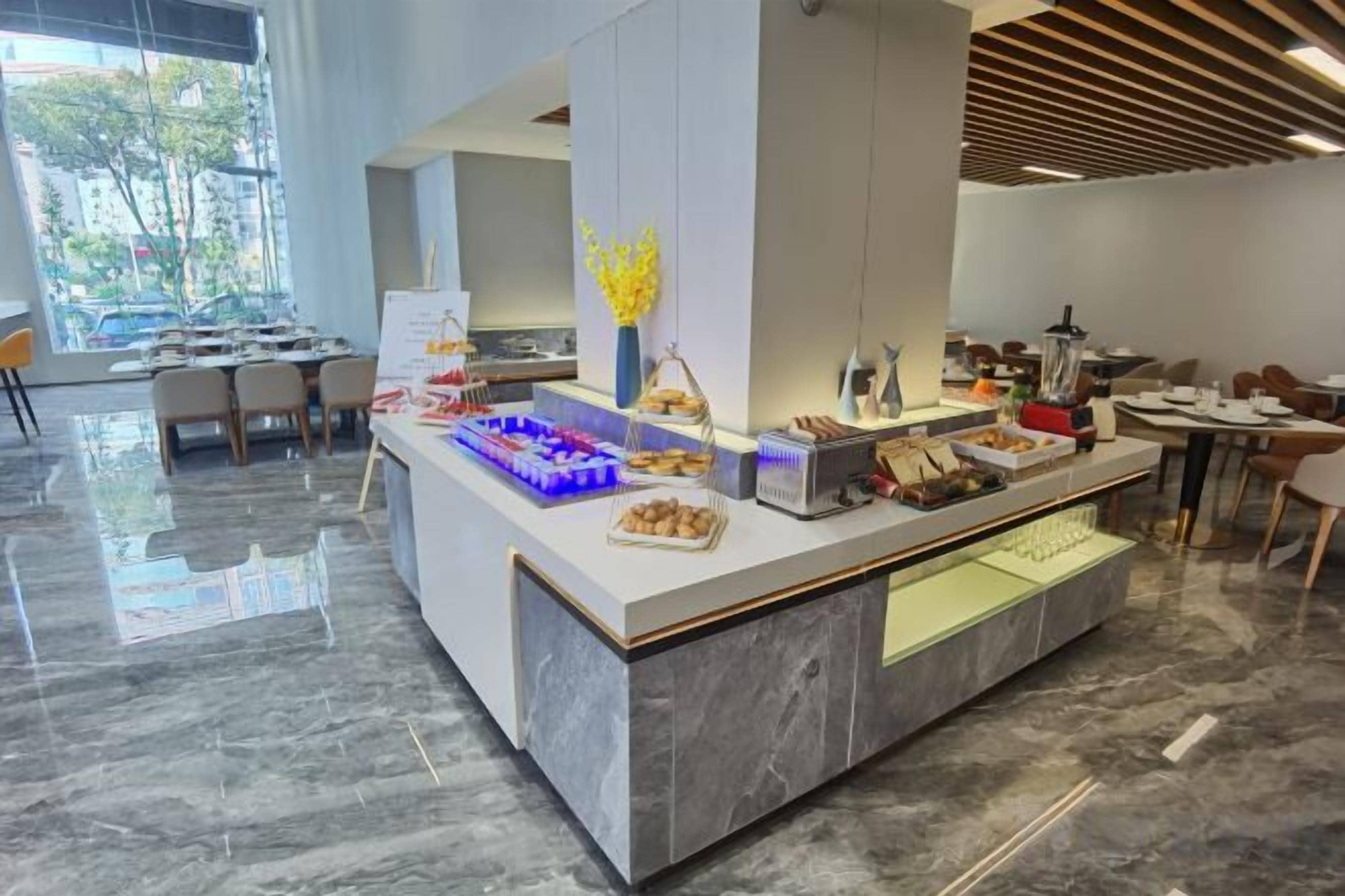 Un comedor moderno con piso de mármol, una barra de buffet con diferentes alimentos y vista al exterior.