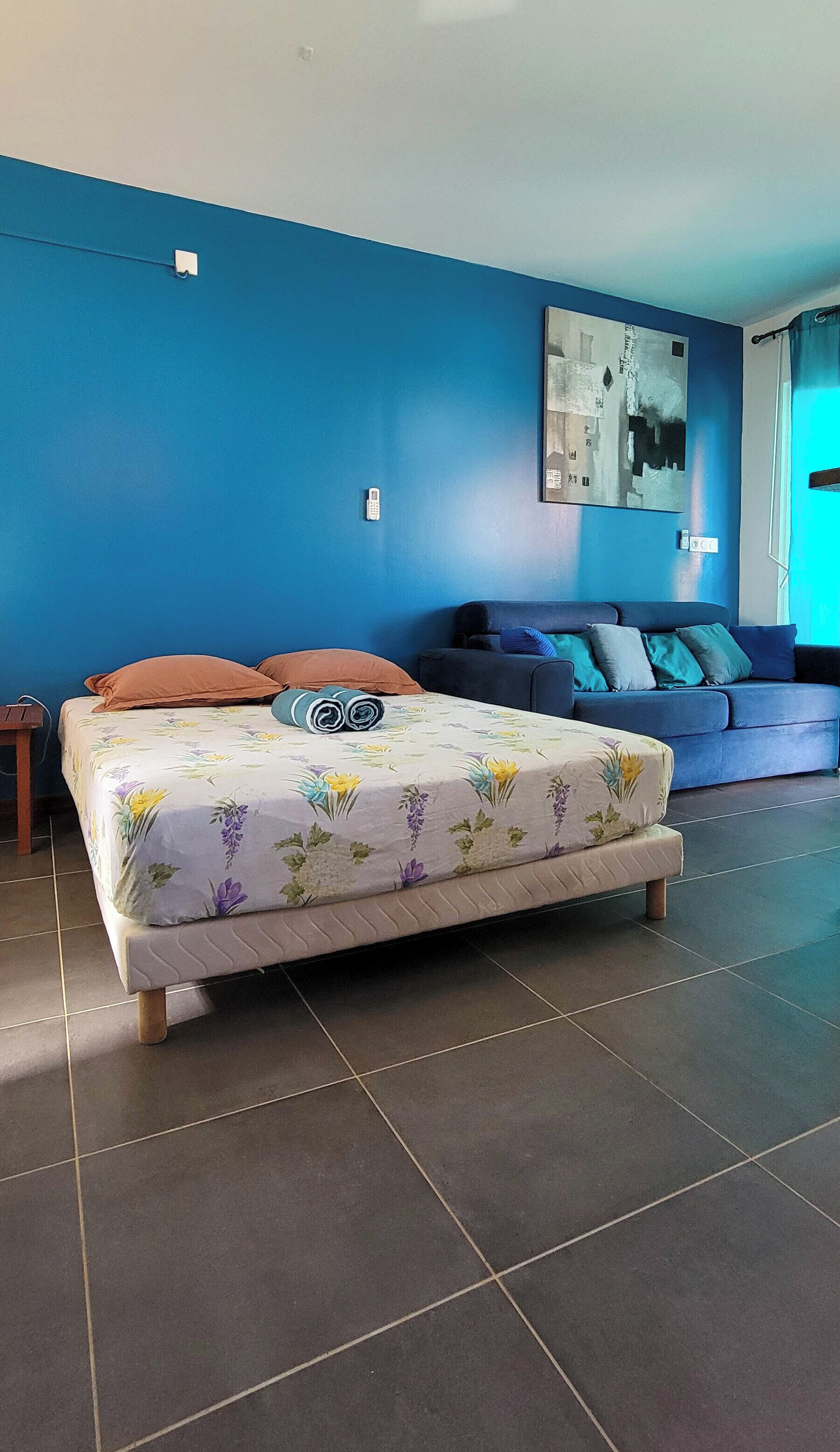 A bedroom with a bed, a sofa, and a wall-mounted artwork.