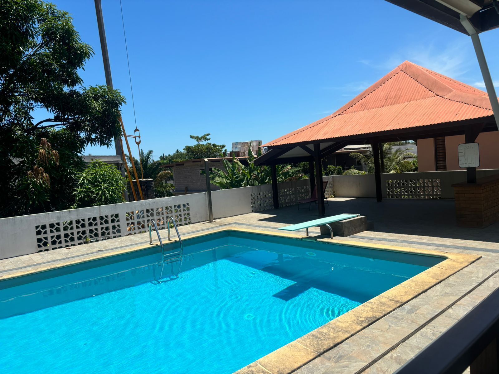 A swimming pool with a tiled deck, a covered seating area, and a view of surrounding greenery.