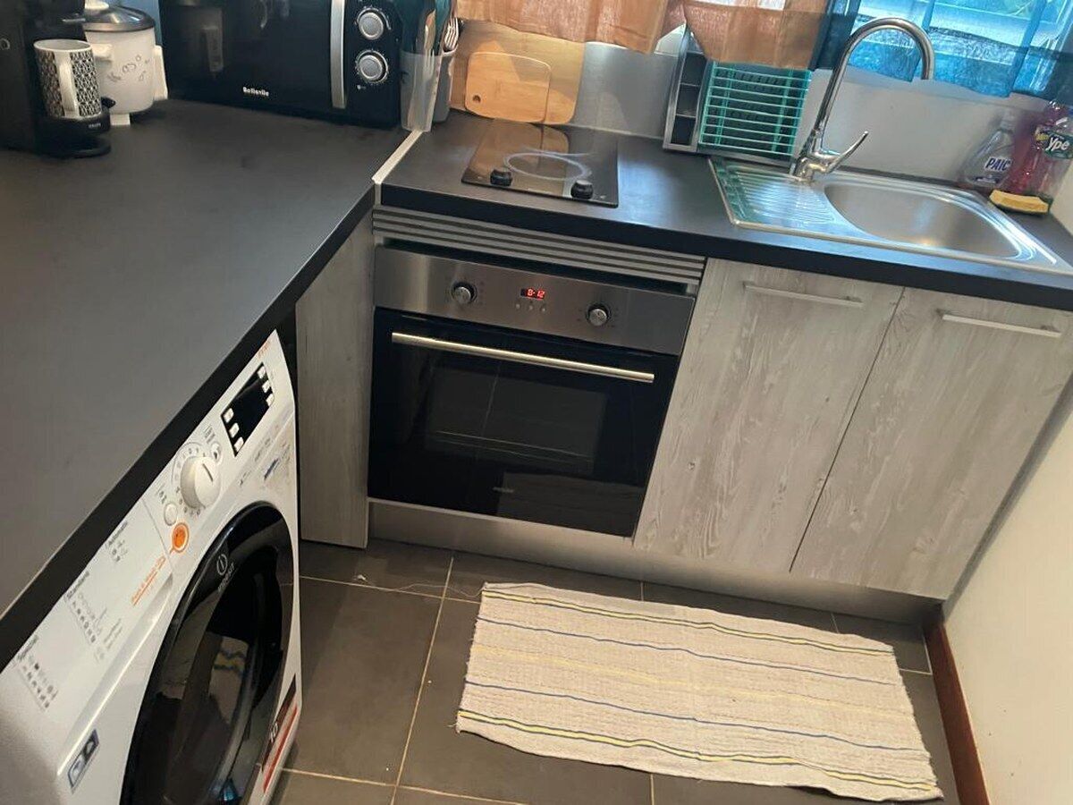 A compact kitchen with a washing machine, oven, and a small countertop with a toaster and kettle.