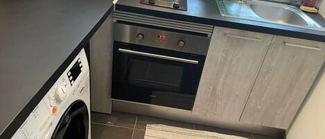 A compact kitchen with a washing machine, oven, and a small countertop with a toaster and kettle.