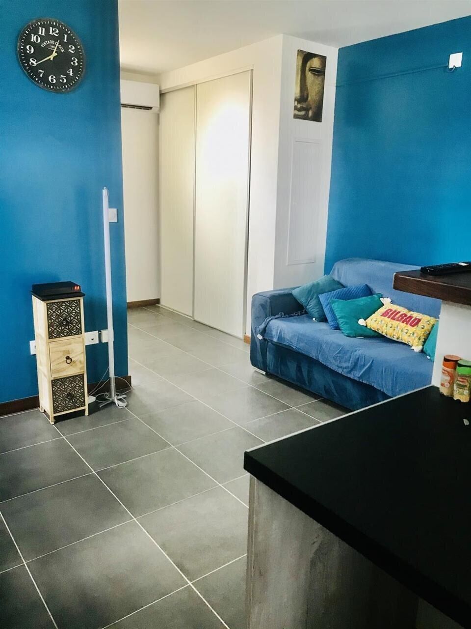 Una habitación con pared azul, un reloj, un sofá con almohadas, un mueble pequeño y una encimera.