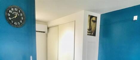 Una habitación con pared azul, un reloj, un sofá con almohadas, un mueble pequeño y una encimera.