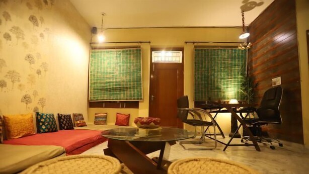 A cozy living room with a sofa, a round coffee table, and two wicker chairs. There is a dining table with chairs and a small kitchen area with a refrigerator.